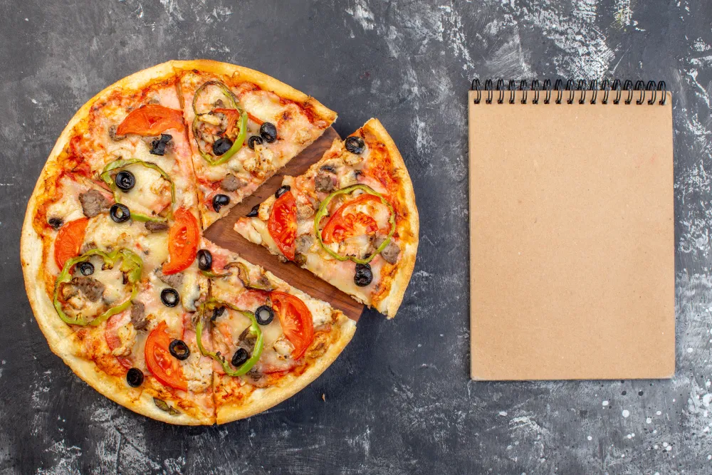 Aufgeschnittene Pizza neben einem leeren Notizblock