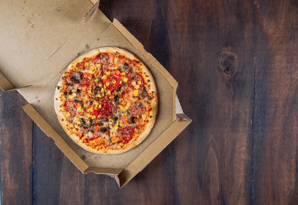 Geöffneter Pizzakarton mit Pizza auf einem Holztisch